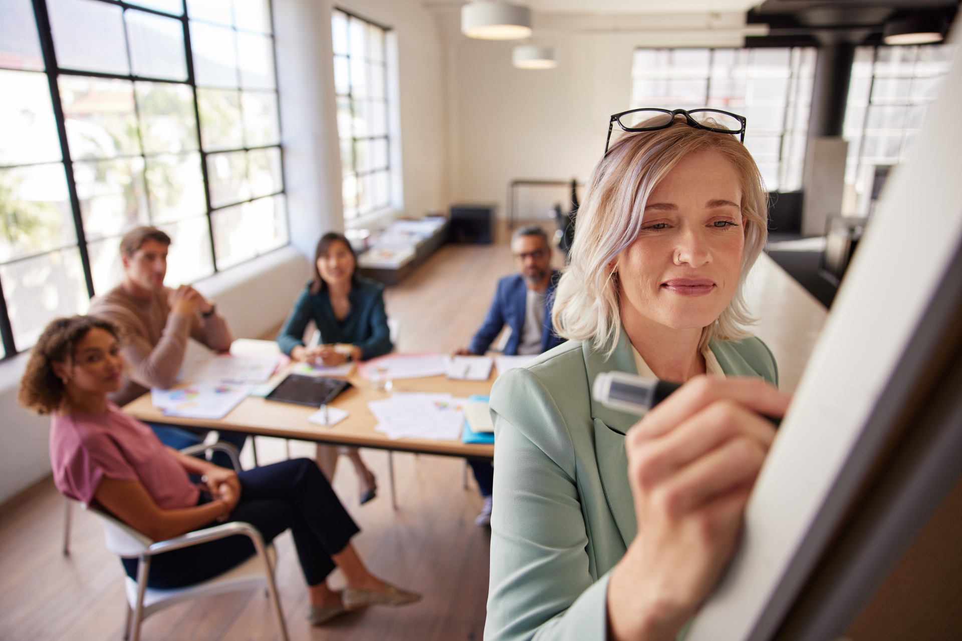 Woman writing on board while team meets
